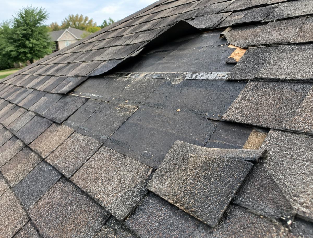 Missing and creased asphalt shingles exposing underlayment on a Texas roof after a windstorm