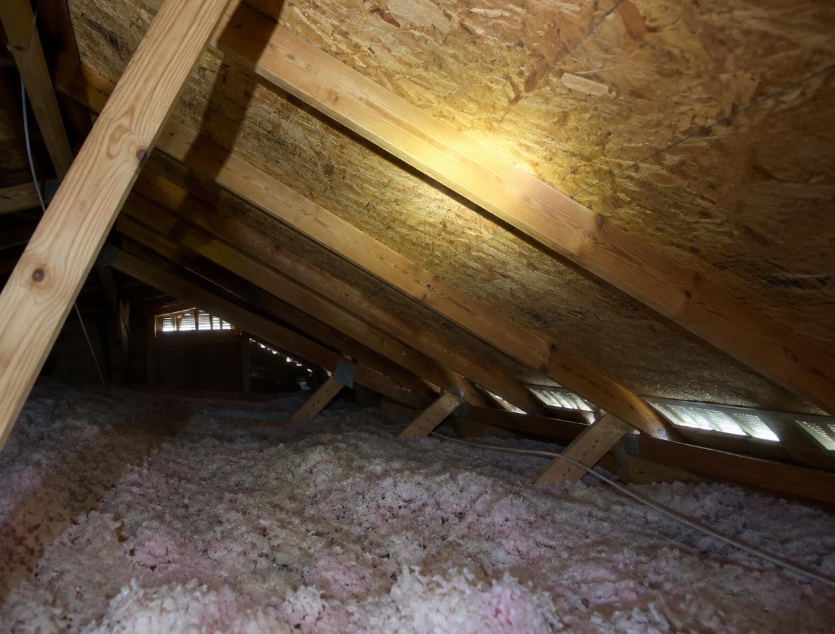 Attic of a Texas home with a flashlight on the roof decking, rafters, insulation, and soffit vents