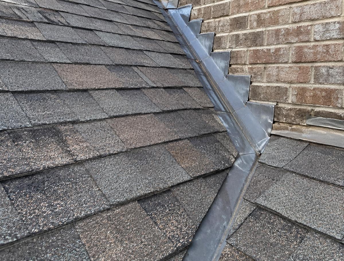 Architectural shingles meeting a brick wall with step flashing and a valley on a Texas home